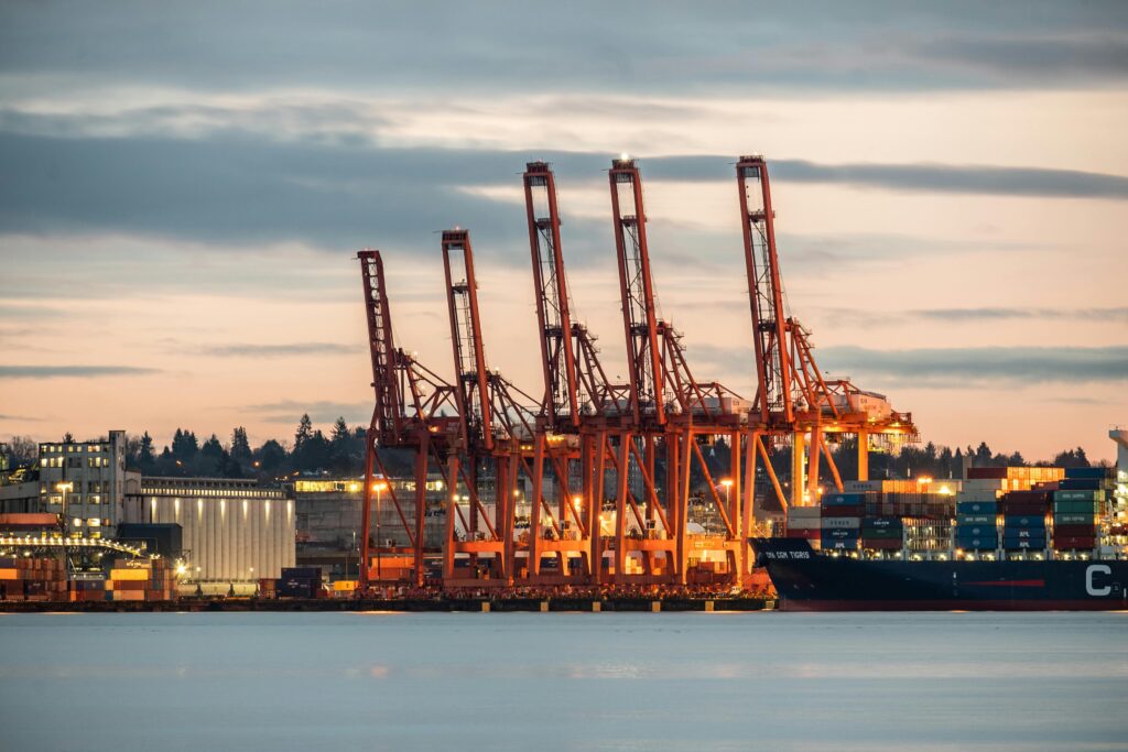 View of industrial cranes and cargo containers at Vancouver Port during sunset, showcasing bustling trade and commerce.